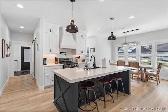 kitchen featuring stainless steel gas range, custom range hood, sink, light hardwood / wood-style floors, and white cabinetry