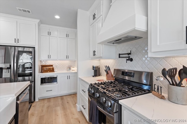 kitchen with premium range hood, light hardwood / wood-style flooring, tasteful backsplash, white cabinetry, and stainless steel appliances