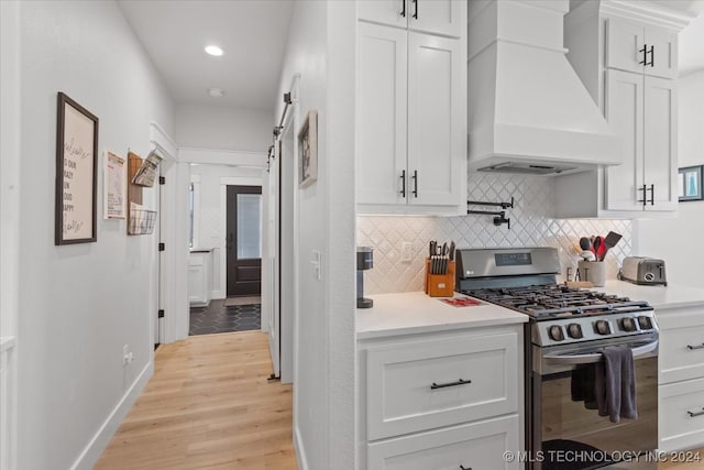 kitchen with custom exhaust hood, light wood-type flooring, tasteful backsplash, white cabinetry, and stainless steel range with gas stovetop