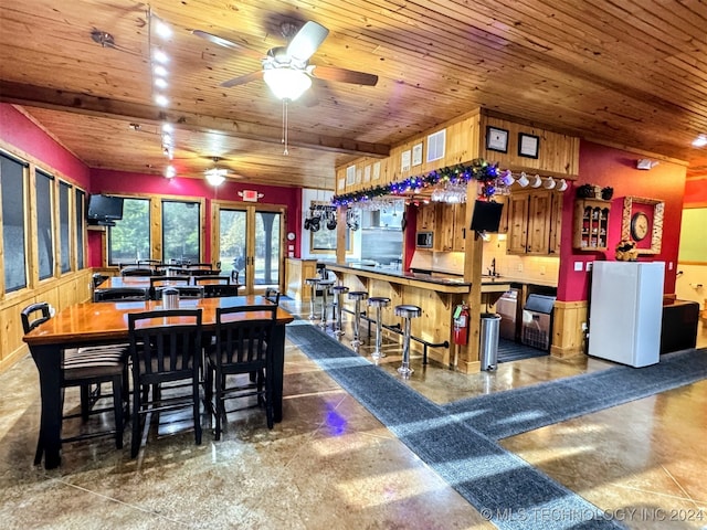 dining space with ceiling fan, beam ceiling, wooden ceiling, and bar area