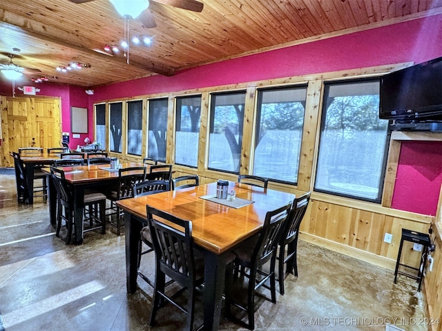 dining room featuring concrete flooring, ceiling fan, wooden ceiling, and wood walls