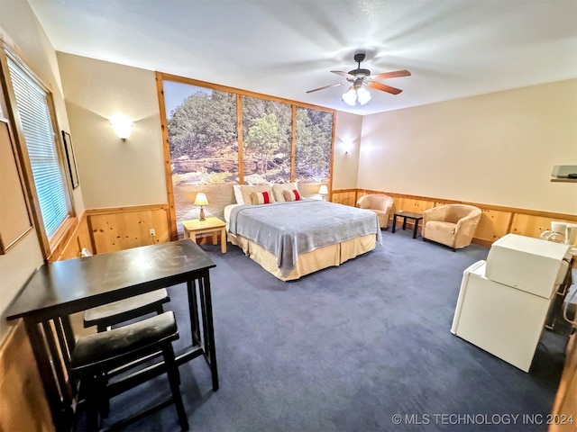 bedroom with ceiling fan, wood walls, and dark carpet