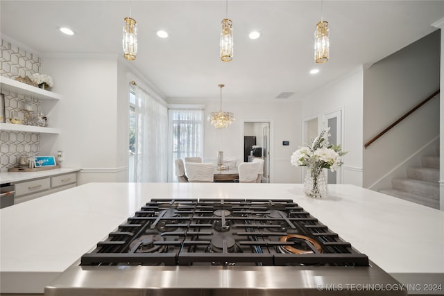 kitchen featuring tasteful backsplash, ornamental molding, pendant lighting, a notable chandelier, and stainless steel gas stovetop