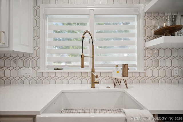 interior details with backsplash, white cabinetry, and sink