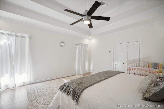 bedroom featuring ornamental molding, a tray ceiling, ceiling fan, light hardwood / wood-style floors, and a closet