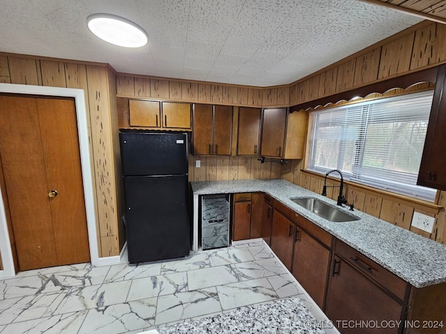 kitchen with wine cooler, wood walls, black refrigerator, and sink