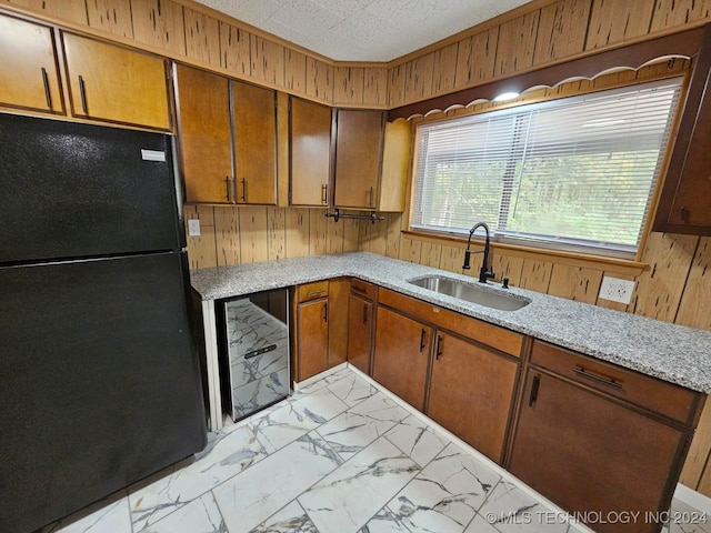 kitchen with black refrigerator, light stone counters, wood walls, and sink