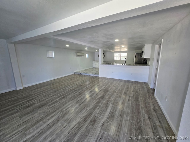 unfurnished living room featuring a wall unit AC, dark wood-type flooring, and a textured ceiling