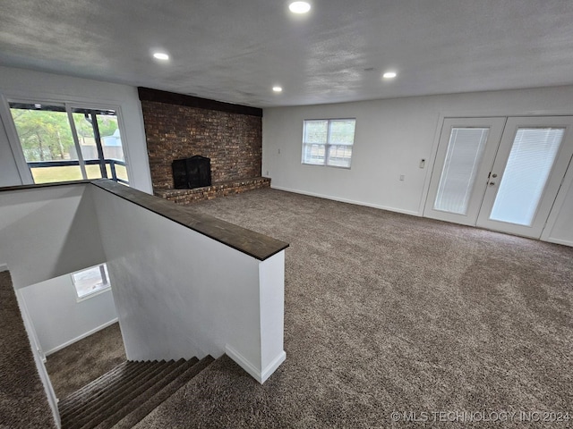 unfurnished living room featuring a textured ceiling, carpet floors, a fireplace, and french doors