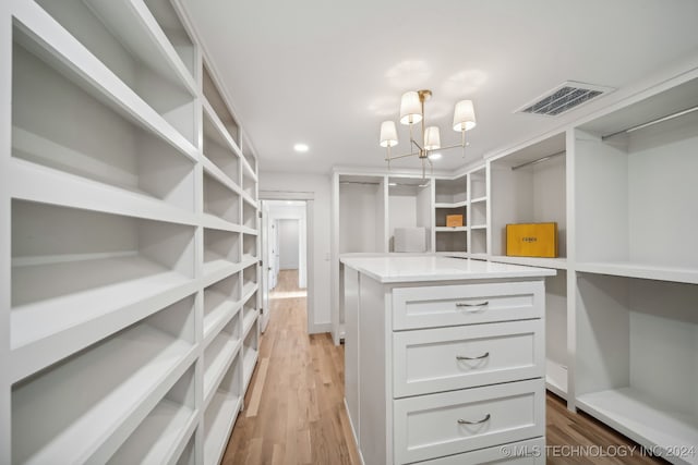 spacious closet with light hardwood / wood-style flooring and a notable chandelier