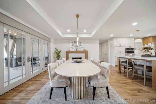 dining space with light hardwood / wood-style floors, a tray ceiling, and french doors