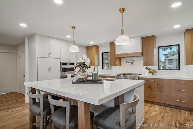 kitchen featuring backsplash, light stone counters, decorative light fixtures, light hardwood / wood-style flooring, and white cabinetry