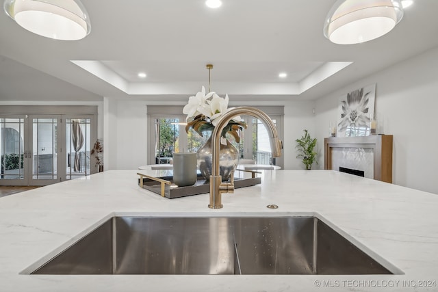 kitchen with light stone countertops, french doors, a raised ceiling, and sink