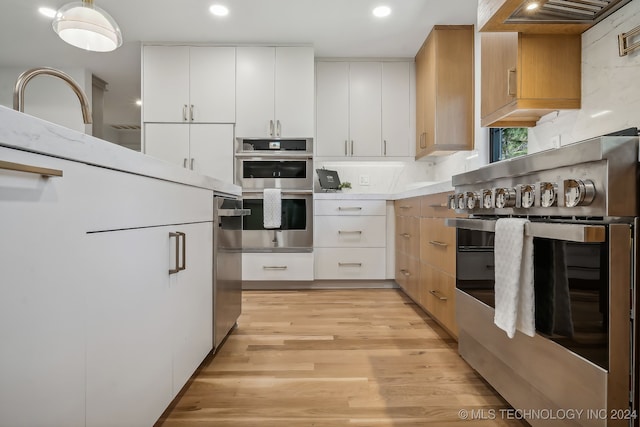 kitchen with white cabinets, appliances with stainless steel finishes, light hardwood / wood-style flooring, and custom range hood