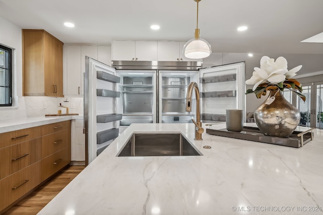 kitchen featuring pendant lighting, white cabinets, sink, light wood-type flooring, and light stone countertops