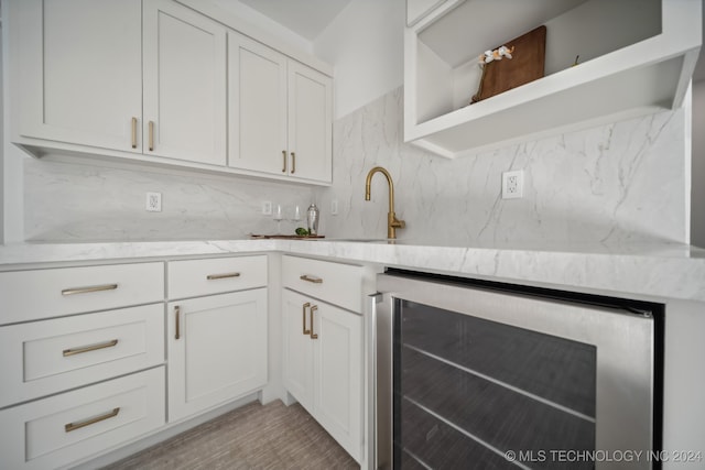 kitchen with backsplash, white cabinetry, beverage cooler, and light wood-type flooring