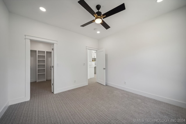 unfurnished bedroom featuring light carpet, a walk in closet, a closet, and ceiling fan