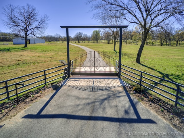 view of gate with a lawn and a rural view