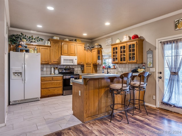 kitchen featuring kitchen peninsula, light wood-type flooring, ornamental molding, a breakfast bar, and white appliances