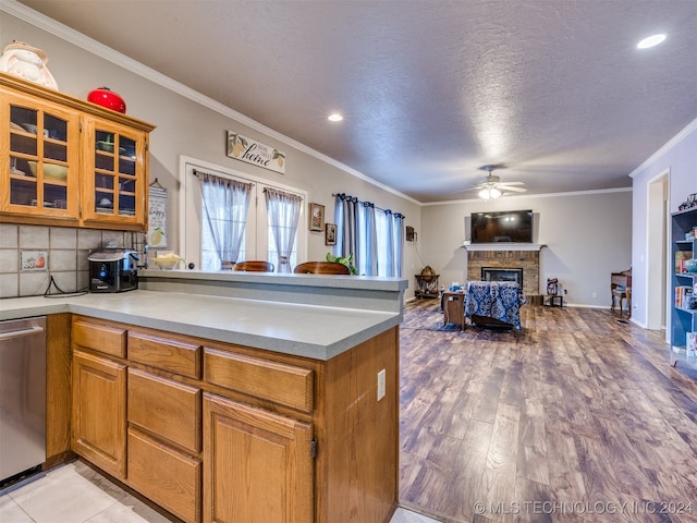 kitchen with stainless steel dishwasher, ceiling fan, crown molding, a fireplace, and light hardwood / wood-style floors