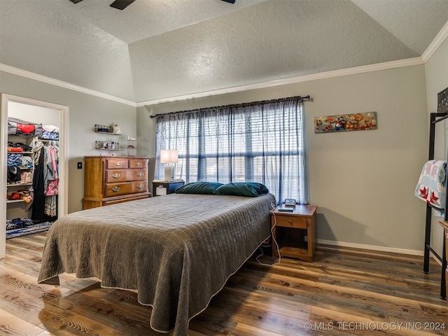 bedroom with a spacious closet, dark wood-type flooring, crown molding, lofted ceiling, and a closet