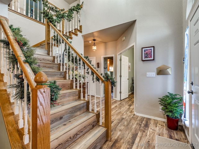 foyer entrance featuring stairs, wood finished floors, a towering ceiling, and baseboards