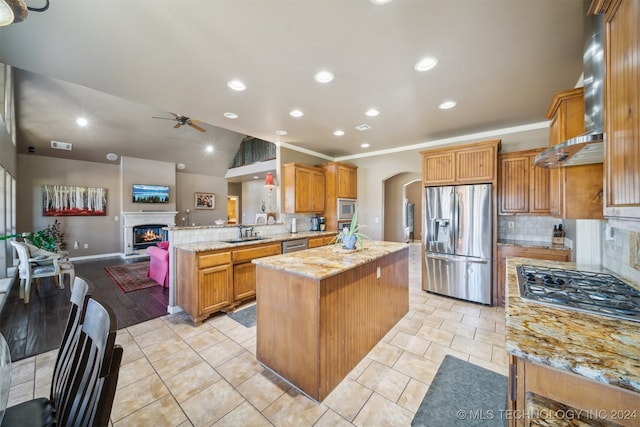 kitchen featuring kitchen peninsula, appliances with stainless steel finishes, backsplash, light stone countertops, and ceiling fan