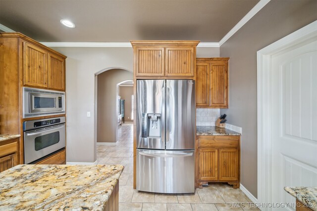 kitchen with light stone counters, appliances with stainless steel finishes, decorative backsplash, light tile patterned floors, and ornamental molding