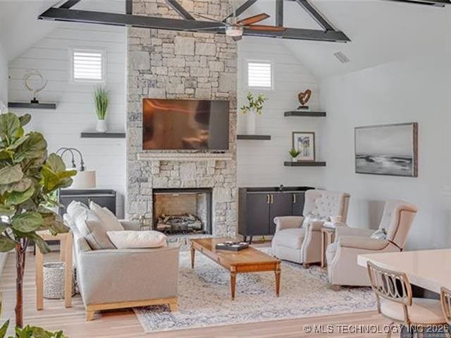 living room with a stone fireplace, ceiling fan, hardwood / wood-style floors, and lofted ceiling with beams