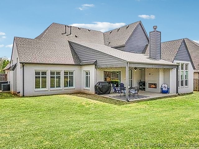 rear view of house with a lawn, a patio, fence, a shingled roof, and a chimney