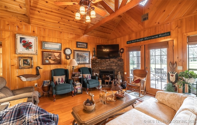 living room featuring beam ceiling, a stone fireplace, wood walls, and light hardwood / wood-style flooring