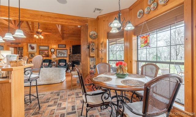 dining area with beamed ceiling, ceiling fan with notable chandelier, wood-type flooring, and wooden walls