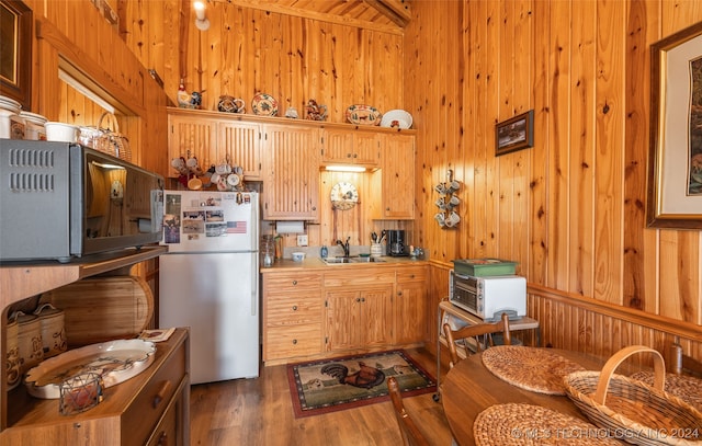 kitchen with white fridge, sink, dark wood-type flooring, and wooden walls