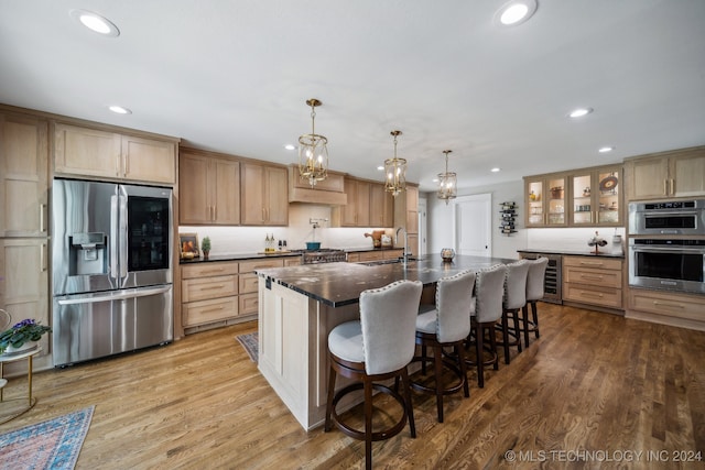 kitchen with hanging light fixtures, beverage cooler, stainless steel appliances, light hardwood / wood-style floors, and a center island with sink