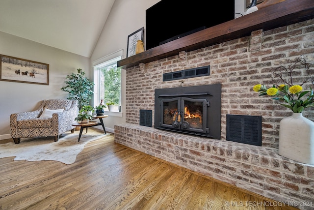 living room featuring hardwood / wood-style floors, high vaulted ceiling, and a brick fireplace