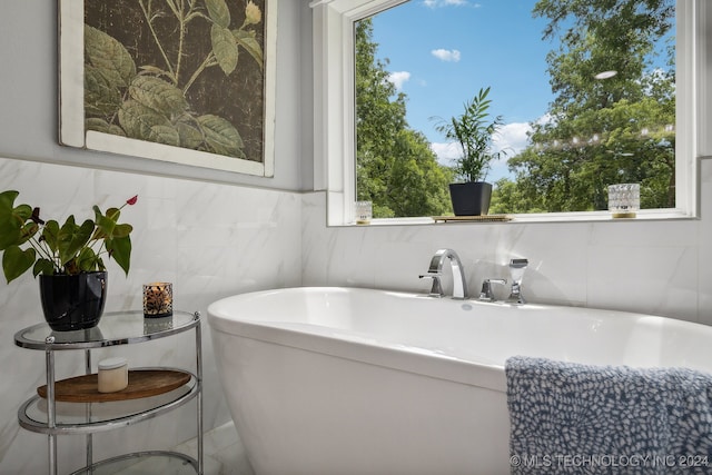 bathroom with plenty of natural light, a bathing tub, and tile walls