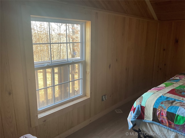 bedroom with wood-type flooring, wooden walls, and multiple windows