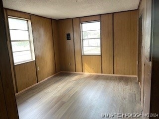 unfurnished room with wood walls, light wood-type flooring, and a textured ceiling