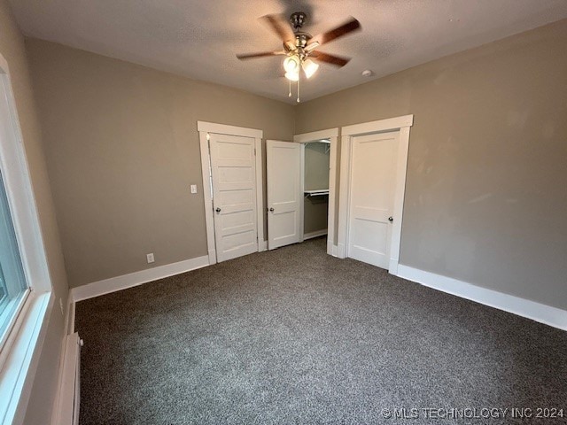 unfurnished bedroom with baseboard heating, ceiling fan, dark carpet, and a textured ceiling