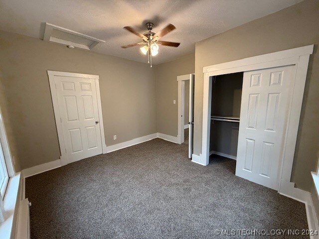 unfurnished bedroom featuring baseboard heating, ceiling fan, a closet, and dark colored carpet