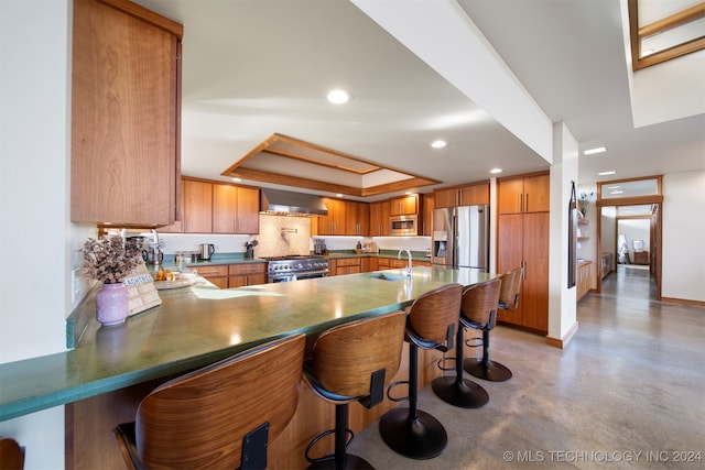 kitchen featuring wall chimney range hood, sink, a breakfast bar area, kitchen peninsula, and stainless steel appliances