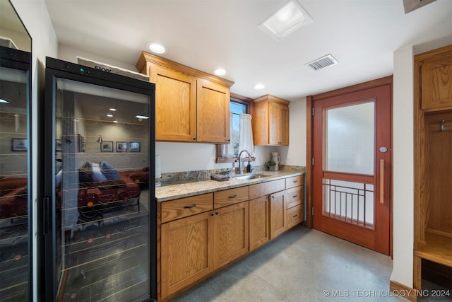 kitchen with light stone counters, wine cooler, and sink