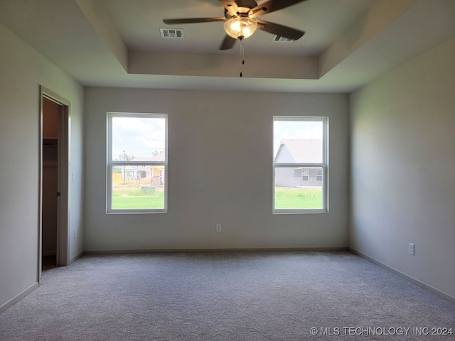 carpeted empty room with a raised ceiling and ceiling fan