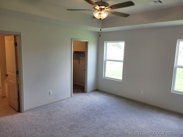 unfurnished bedroom with light carpet, a walk in closet, and ceiling fan