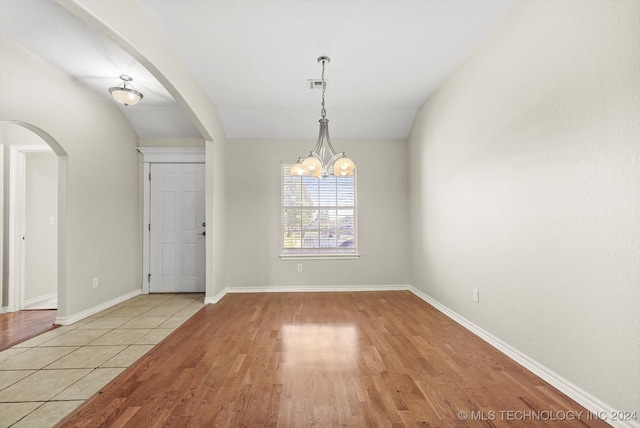 spare room featuring an inviting chandelier, lofted ceiling, and light wood-type flooring