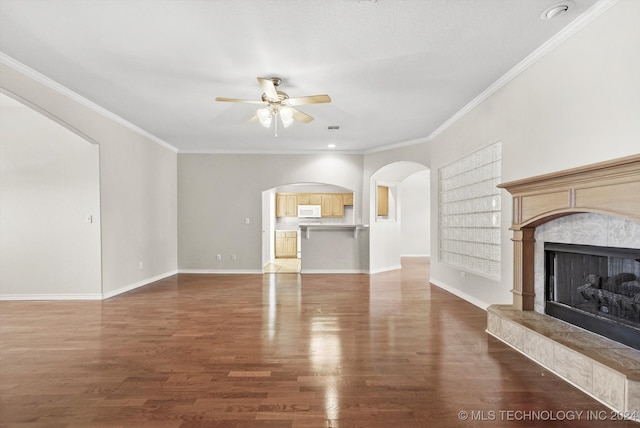 unfurnished living room featuring wood-type flooring, ceiling fan, crown molding, and a tiled fireplace