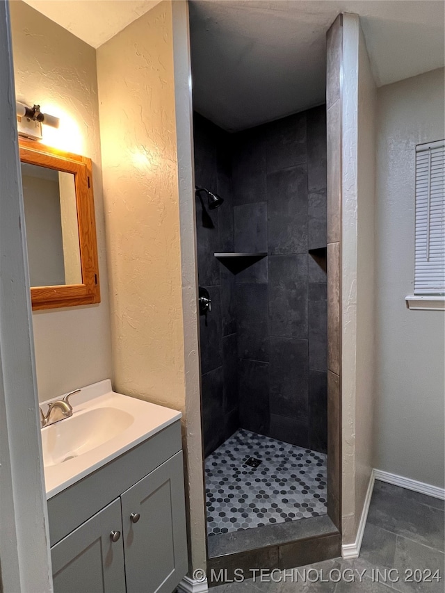 bathroom with tile patterned flooring, a tile shower, and vanity