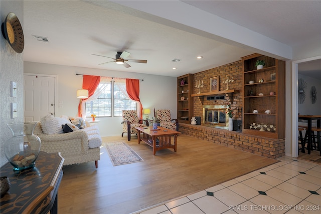 living room with ceiling fan, light hardwood / wood-style flooring, built in features, and a brick fireplace