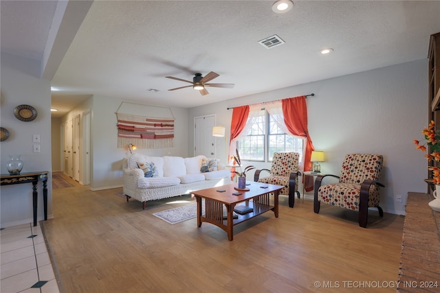 living room featuring ceiling fan, a textured ceiling, and light wood-type flooring