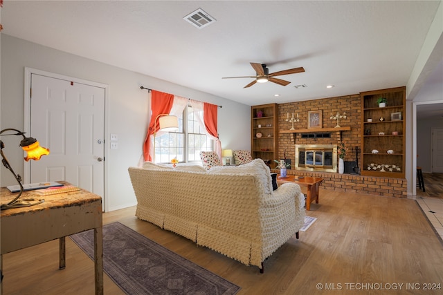 living room featuring built in features, wood-type flooring, a brick fireplace, and ceiling fan